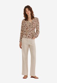 Langærmet mønstret bluse i creme med blomster mønstre, parret med lyse beige vide bukser og flade sandaler.