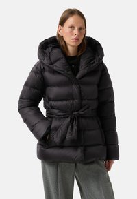 Sort pufferjakke med en stor hætte, samlede taljeledninger og quiltet design. Stoffet ser skinnende ud med sidelommer og trykknaplukninger.