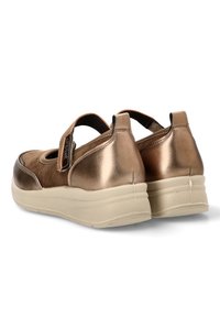 Zapatos de color bronce con un acabado metálico brillante y acentos de ante. Cuentan con una correa de Velcro y una suela gruesa de textura beige.