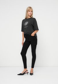 Zwarte cargobroek met een aansluitend ontwerp, zijzakken en een grijs oversized t-shirt met een zonafbeelding in het wit. Zwarte slingback-hakken.