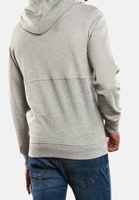 Sweat à capuche gris en tissu texturé, avec une capuche à cordon de serrage et des poignets côtelés. Associé à un jean en denim bleu.