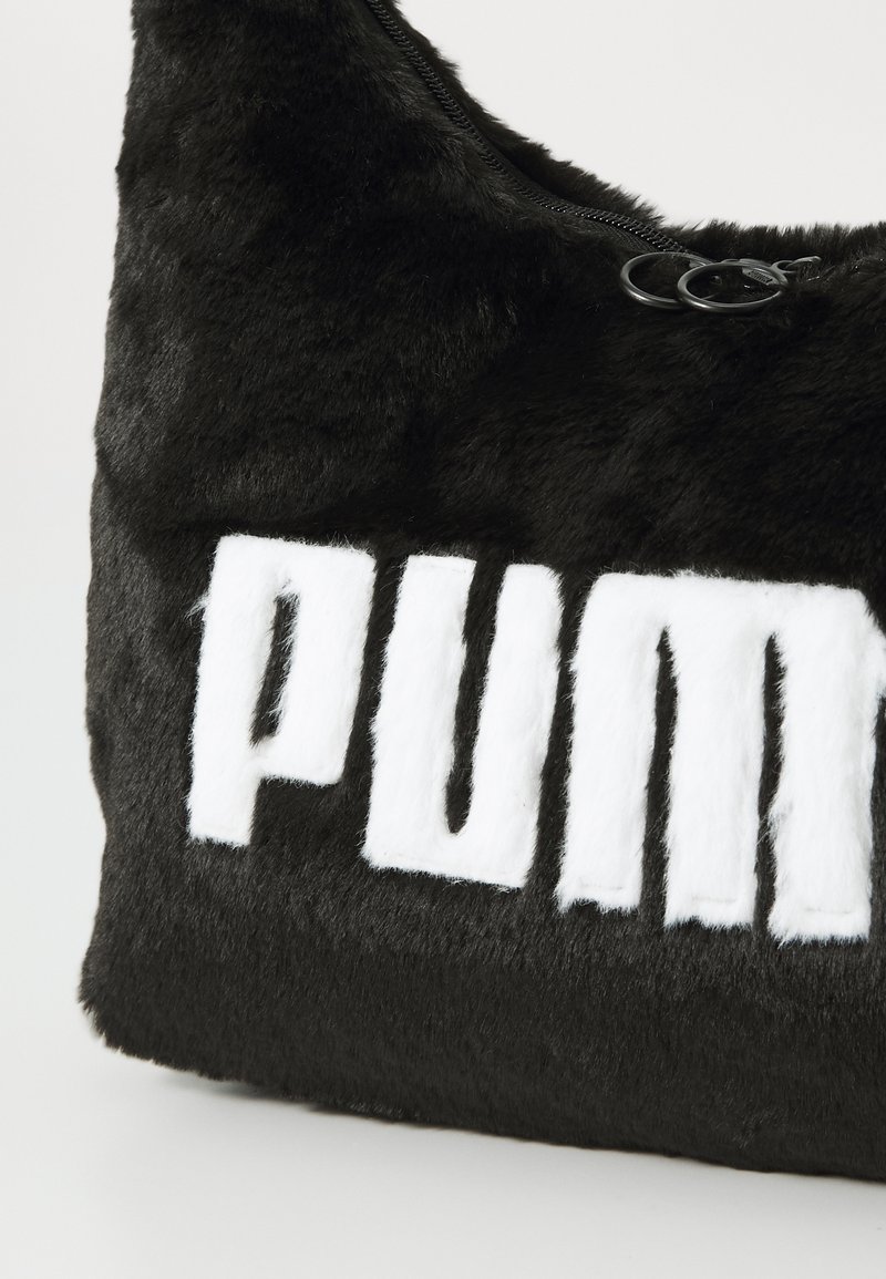 Bolso de hombro de piel sintética negra con un atrevido logo blanco de "PUMA". Incluye un cierre de cremallera y una textura suave. Diseño compacto y curvado.