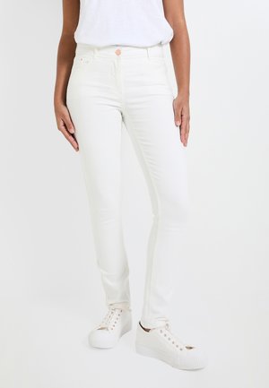 Jeans skinny blancos de mezclilla, con una cintura alta, diseño de cinco bolsillos y un botón rosa sutil. Combinados con zapatillas blancas.