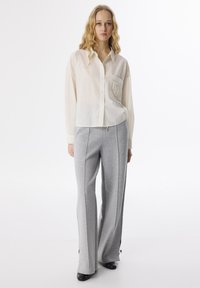 Chemise boutonnée beige clair avec une poche carrée et un pantalon large gris, fabriquée en tissu doux, avec une texture lisse et des détails subtils.