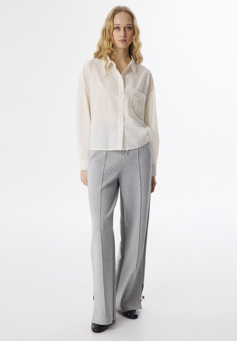 Chemise boutonnée beige clair avec une poche carrée et un pantalon large gris, fabriquée en tissu doux, avec une texture lisse et des détails subtils.