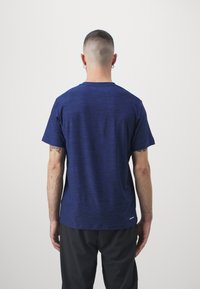 Navy blue short-sleeve t-shirt with a heathered texture, crew neck, and a small logo trim at the hem, worn with black pants.