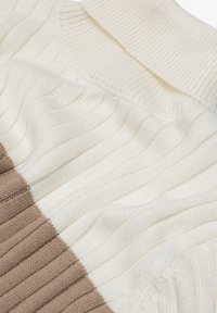 Neulepaita vaaleassa kerma- ja vaaleansruskeassa, jossa on ribbitekstuuri aaltoilevilla kuvioilla ja kontrastoivilla osioilla vaakaraidoissa.