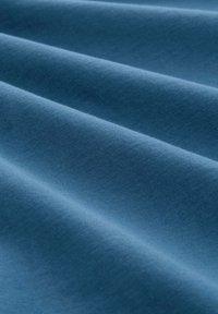 Blaues Baumwollgewebe mit einer glatten Textur, das sanfte Falten aufweist, die weiche Schatten erzeugen und dessen Gewicht und Flexibilität betonen.