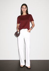 Burgundy short-sleeve t-shirt paired with high-waisted white wide-leg trousers. Accessorized with a brown woven handbag and a watch.