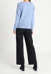 Ljusblå, fluffig stickad tröja med avslappnad passform och rak nederkant, tillsammans med lösa svarta byxor och svarta högklackade skor.