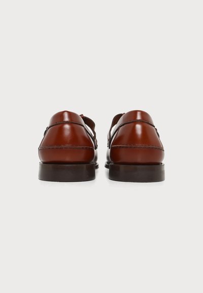Paire de chaussures habillées en cuir marron poli, vues de dos avec des semelles noires sur un fond clair uni.