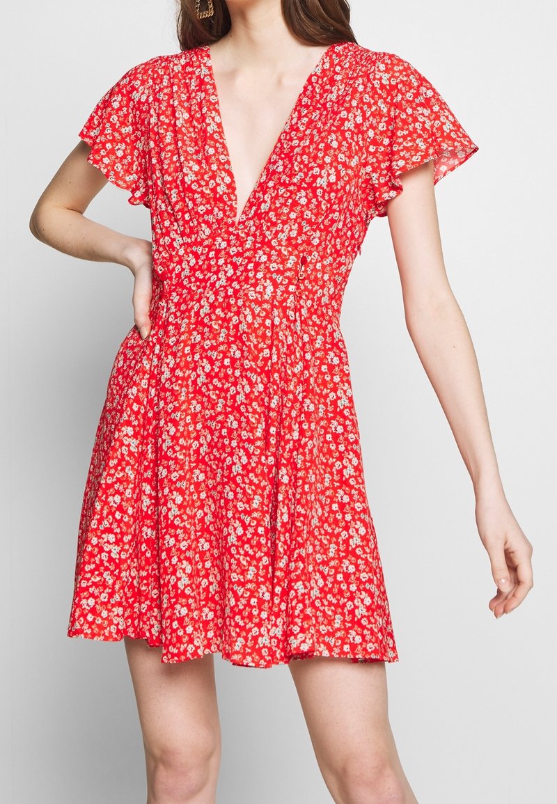 Vestido rojo floral con un escote en V profundo, mangas cortas de volantes y un cuerpo ajustado que fluye hacia una falda acampanada. Tejido ligero y texturizado.