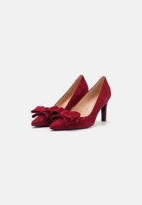 Escarpins rouges en suède avec un bout pointu et un grand nœud accent à l'avant, dotés d'un élégant talon aiguille noir.
