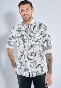 Weißes Hemd mit schwarzen botanischen Drucken, kurzen Ärmeln, Knopfkragen, Brusttasche und aufgerollten Manschetten. Der Stoff hat eine strukturierte Oberfläche.