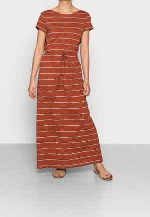 Kobieta ubrana w rdzawobrązową, krótkorękawową sukienkę sięgającą kostek z białymi poziomymi paskami i sznurkiem w pasie, w połączeniu z beżowymi sandałami.