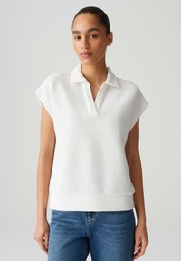 Polo bianco a maniche corte realizzato in tessuto testurizzato, con colletto e una vestibilità rilassata, abbinato a jeans in denim blu.