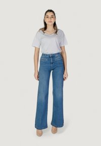 Jeans azules de talle alto con piernas anchas, combinados con una camiseta blanca de cuello en V. El denim tiene una textura suave y un detalle mínimo.