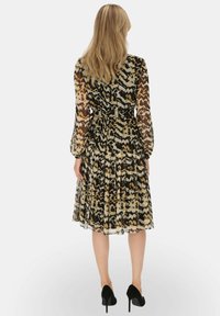 Sukienka do kolan w kwiatowy wzór, wykonana z przezroczystego materiału, z długimi rękawami, dopasowaną talią, rozkloszowanym dołem i falbaną na krawędzi. W kolorach czarnym i beżowym.
