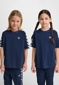 Magliette in cotone blu navy con strisce a zigzag bianche sulle maniche e un piccolo logo sul petto, abbinate a pantaloni della tuta blu navy coordinati.