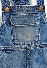 Vaaleansiniset farkkuhaalarit, joissa on säädettävät olkaimet, etutasku ja vastakkaiset ruskeat tikkausompeleet. Kulumista koko vaatteessa.