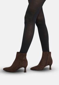 Botines de ante marrón con punta puntiaguda, tacón bajo tipo kitten y cremallera lateral. La textura es suave, con un acabado liso y sin patrones visibles.