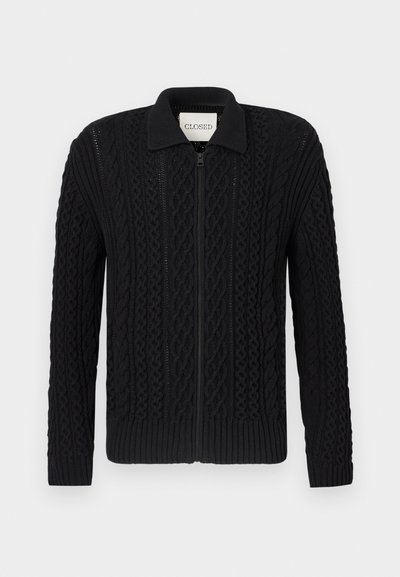 Cardigan noir en maille tricotée avec une fermeture éclair, présentant un motif en torsades texturé, des poignets côtelés et un col.