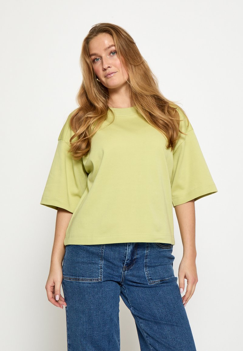 Top in cotone verde chiaro a maniche corte con vestibilità rilassata e scollo rotondo, abbinato a jeans blu a vita alta con gambe larghe.