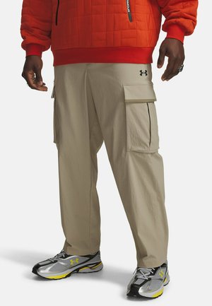Beige cargo pants with side pockets, lightweight fabric, and fitted design. Paired with black and silver athletic shoes featuring yellow accents.
