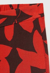 Red fabric featuring large dark brown leaf patterns, with an elastic waistband and a smooth texture.