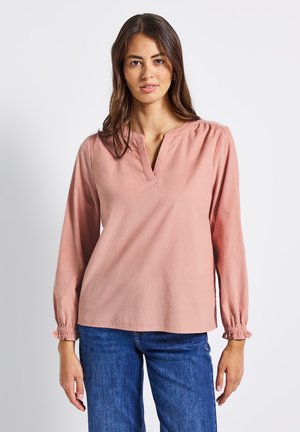 Chemise à manches longues rose clair avec un col en V, détails froncés aux épaules et poignets élastiques, associée à un jean en denim bleu.