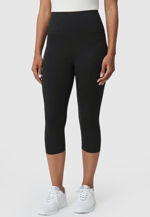 Black knee-length leggings with a high, wide waistband, made from a smooth, stretchy fabric. Paired with white athletic shoes.