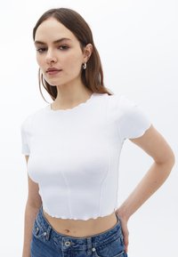 Hvid cropped t-shirt med bølget krave og korte ærmer, der har sømdetaljer. Stylet med højtaljede denimjeans.