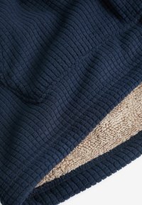 Couverture bleu marine avec un motif côtelé texturé sur un côté et une polaire douce beige au revers, présentant un bord cousu.