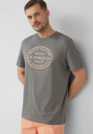 Graues T-Shirt mit kurzen Ärmeln aus Baumwolle, das einen großen ovalen grafischen Druck in blassrosa Text mit Marken- und Standortdetails zeigt.