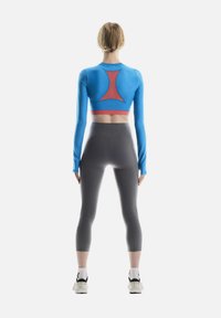 Blue long-sleeve crop top with red accent, paired with high-waisted gray leggings. Model facing away, showcasing fit and design.
