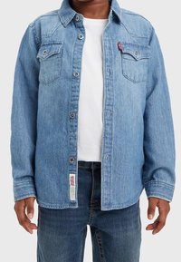 Jasnoniebieska koszula dżinsowa z pointed kołnierzykiem, zapięciem na guziki i dwoma kieszeniami na piersi. Posiada metkę z logo Levi's z boku.