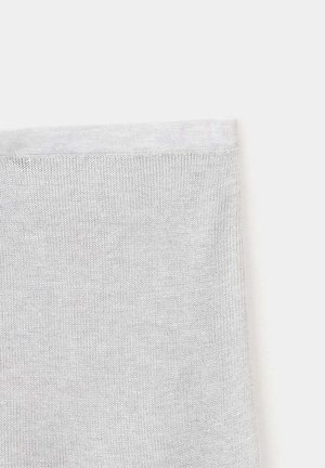 Gros plan d'un tissu tricoté blanc montrant des points fins et réguliers ainsi qu'un bord ourlé sur un fond clair uni.