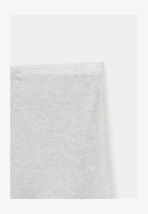 Gros plan d'un tissu tricoté blanc montrant des points fins et réguliers ainsi qu'un bord ourlé sur un fond clair uni.