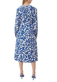 Blau-weiß gemustertes Kleid mit langen Ärmeln, gerafftem Ausschnitt und einer Länge bis zur Mitte der Wade, kombiniert mit blauen High-Heels.