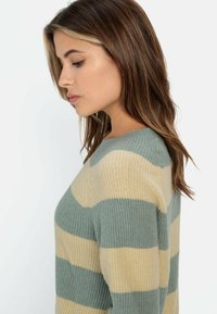 Gestreepte trui in groen en beige, gebreide textuur, met een ronde hals en lange mouwen. Zijaanzicht toont het kleurpatroon en de pasvorm.