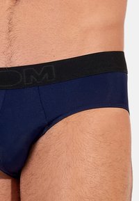 Marineblauwe boxershorts met een zwarte tailleband waarop het logo "DOM." Soepele textuur met een strakke pasvorm en minimale naden voor comfort.