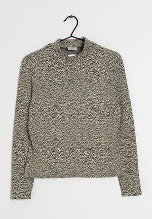 Haut beige à manches longues avec petit motif à points noirs irréguliers, col rond, suspendu sur un cintre noir sur fond blanc.