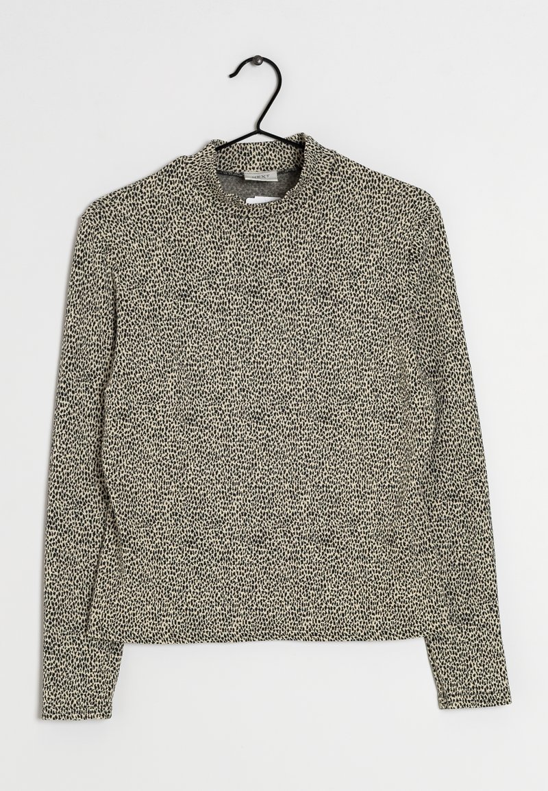 Haut beige à manches longues avec petit motif à points noirs irréguliers, col rond, suspendu sur un cintre noir sur fond blanc.