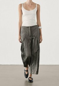 Biała, dopasowana koszulka na ramiączkach w połączeniu z luźnymi, pomarszczonymi, ciemnoszarymi spodniami. Modelka ma na sobie czarne buty na kostkę. Minimalistyczny design.