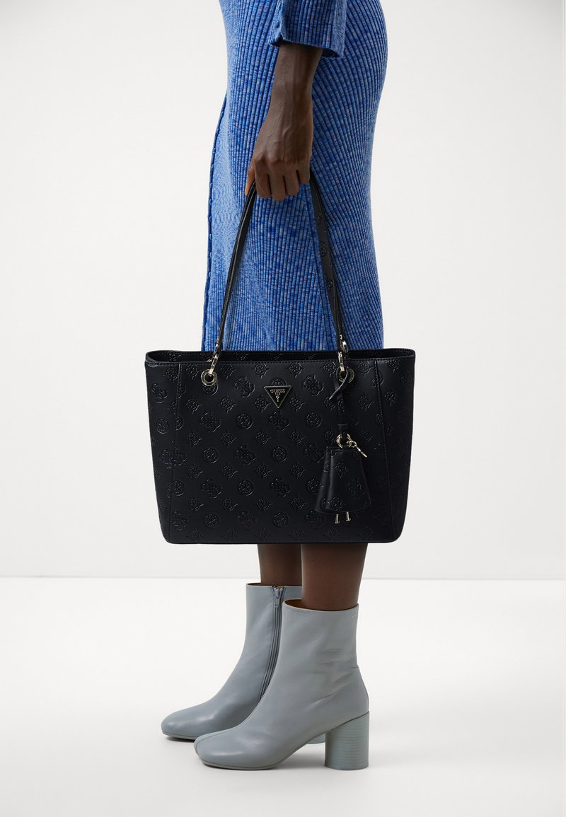 Borsa tote nera con motivo a logo in rilievo, doppio manico e un accento con portachiavi removibile. Presenta una forma strutturata e una texture liscia.