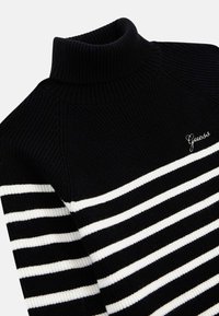 Pull noir à col roulé en tricot avec des rayures blanches horizontales et un petit logo "Guess" brodé sur la poitrine gauche.
