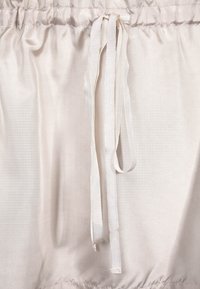 Light beige fabric with a smooth texture and elastic waistband; finished with matching satin drawstrings for adjustment.