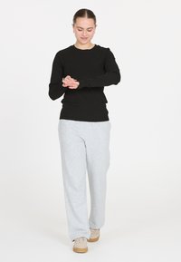 Schwarzes, geripptes Langarmoberteil, kombiniert mit hellgrauen Sweatpants. Die Hose ist locker sitzend, und das Modell trägt beiger Sneakers.