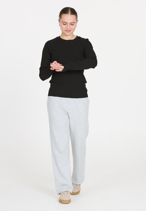 Schwarzes, geripptes Langarmoberteil, kombiniert mit hellgrauen Sweatpants. Die Hose ist locker sitzend, und das Modell trägt beiger Sneakers.
