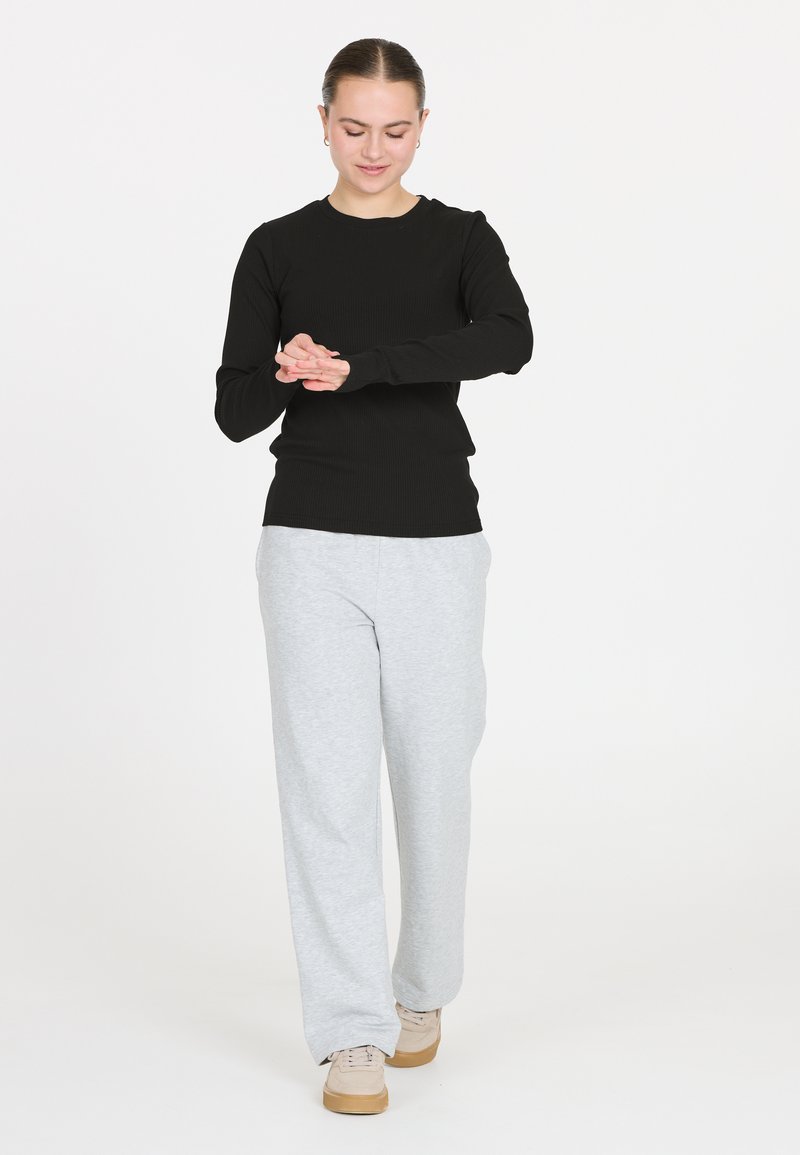 Schwarzes, geripptes Langarmoberteil, kombiniert mit hellgrauen Sweatpants. Die Hose ist locker sitzend, und das Modell trägt beiger Sneakers.